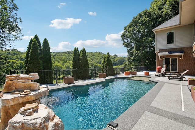 view of swimming pool with a patio area, a view of trees, fence, and a fenced in pool