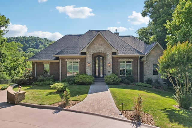 view of front of property with brick siding, a shingled roof, stone siding, french doors, and a front yard