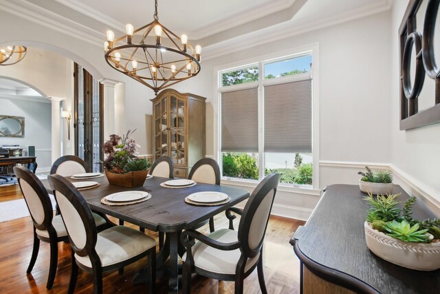 dining area featuring decorative columns, arched walkways, a raised ceiling, crown molding, and light wood-type flooring