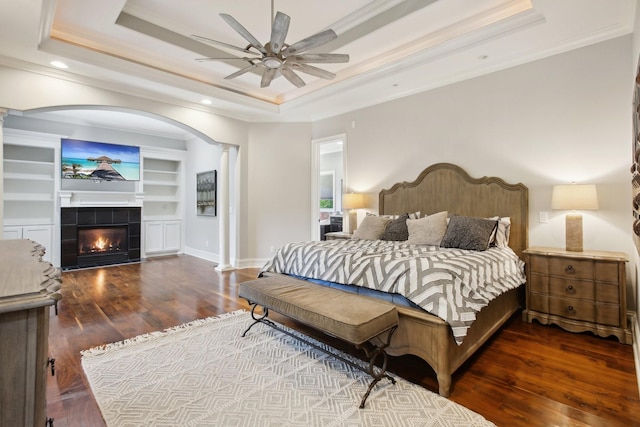 bedroom with ornamental molding, a tray ceiling, a tile fireplace, and wood finished floors