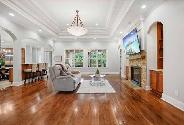 living room featuring a tray ceiling, crown molding, wood-type flooring, a stone fireplace, and baseboards