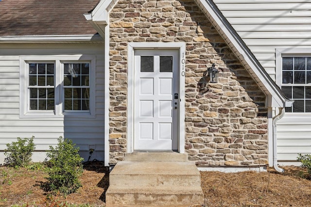 entrance to property with stone siding and a shingled roof