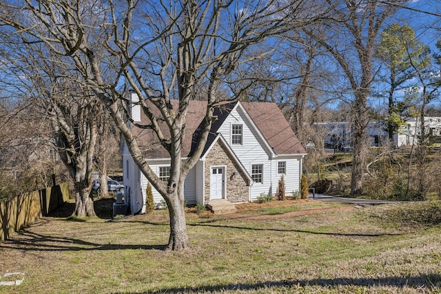 view of front of property with stone siding, roof with shingles, fence, and a front yard