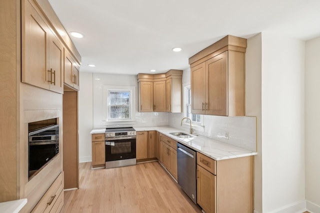 kitchen featuring light stone counters, stainless steel appliances, decorative backsplash, a sink, and light wood-type flooring