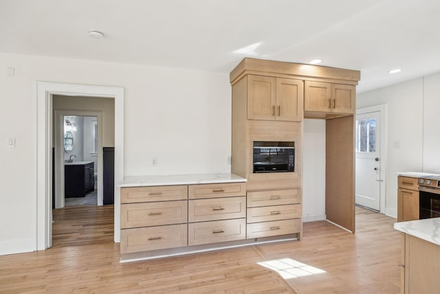 kitchen featuring light wood finished floors, recessed lighting, light brown cabinets, a sink, and light stone countertops