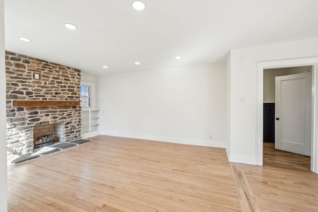 unfurnished living room featuring recessed lighting, a stone fireplace, and light wood-style flooring