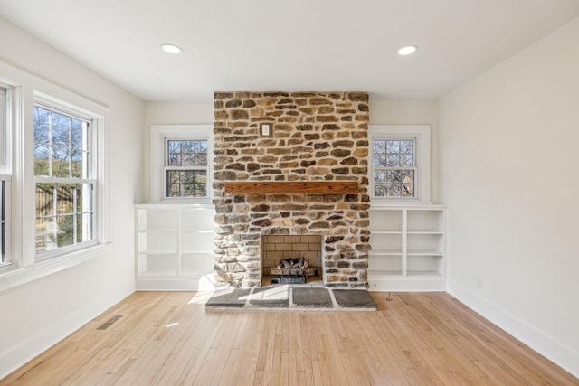 unfurnished living room featuring a large fireplace, wood-type flooring, visible vents, and baseboards