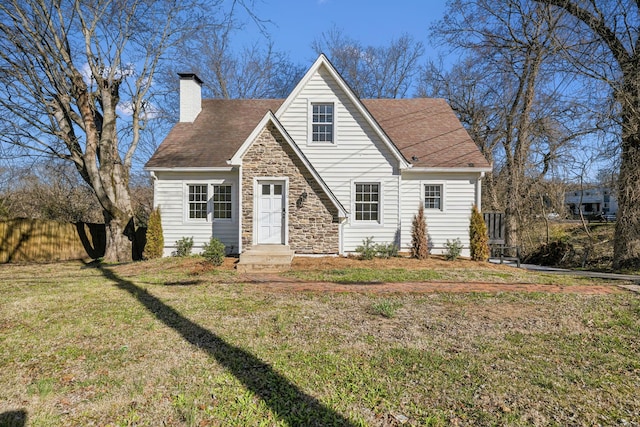 view of front of home with stone siding, a chimney, roof with shingles, fence, and a front yard