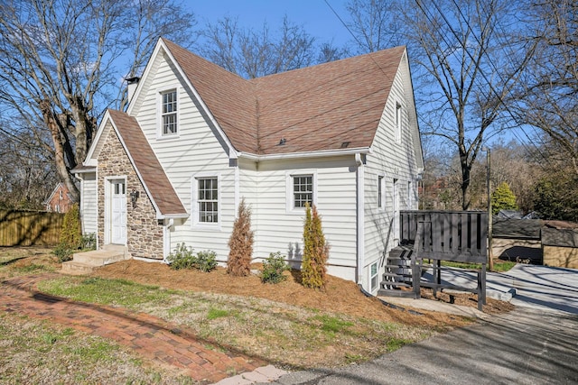 view of side of property featuring stone siding, a shingled roof, and fence