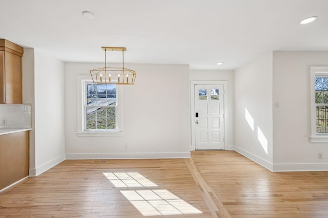 unfurnished dining area featuring light wood-style floors, baseboards, an inviting chandelier, and recessed lighting