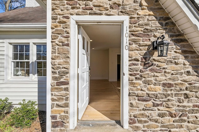 entrance to property featuring a shingled roof and stone siding