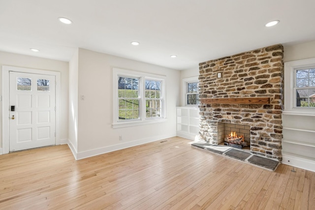 unfurnished living room featuring light wood-style floors, a fireplace, baseboards, and a wealth of natural light