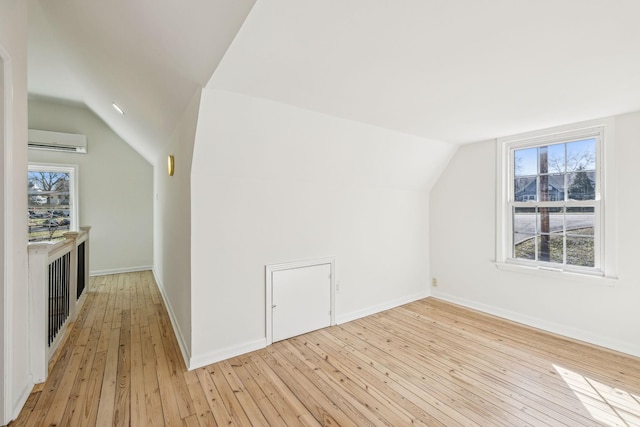 additional living space featuring lofted ceiling, light wood-type flooring, a wall mounted air conditioner, and baseboards