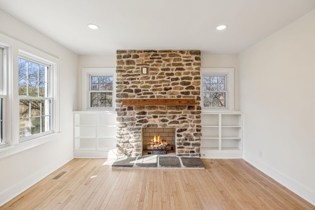 unfurnished living room with a large fireplace, hardwood / wood-style flooring, visible vents, and baseboards