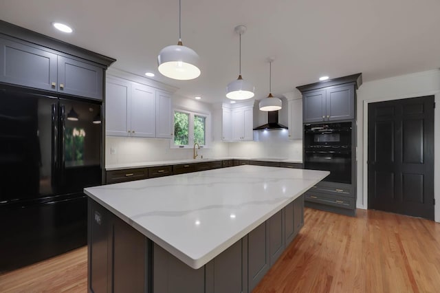 kitchen featuring light wood finished floors, tasteful backsplash, light stone counters, wall chimney range hood, and black appliances