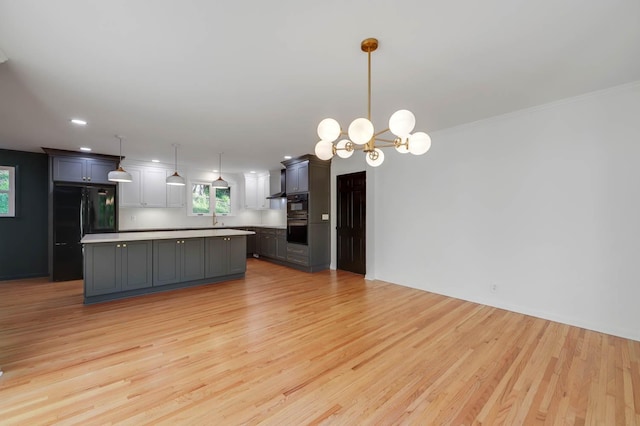 kitchen featuring a notable chandelier, light countertops, light wood-style flooring, freestanding refrigerator, and a kitchen island