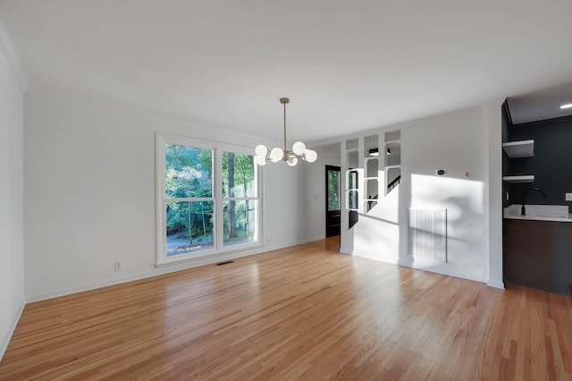 empty room featuring light wood-style flooring, visible vents, a chandelier, and a sink