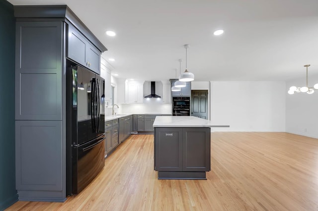 kitchen with light countertops, light wood-style flooring, a sink, black appliances, and wall chimney exhaust hood