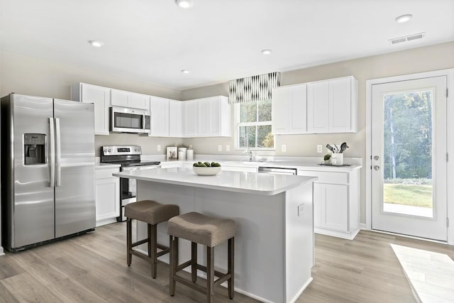 kitchen featuring appliances with stainless steel finishes, white cabinets, a kitchen island, and light wood finished floors