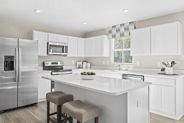 kitchen featuring white cabinets, light wood-style flooring, appliances with stainless steel finishes, a center island, and a kitchen bar