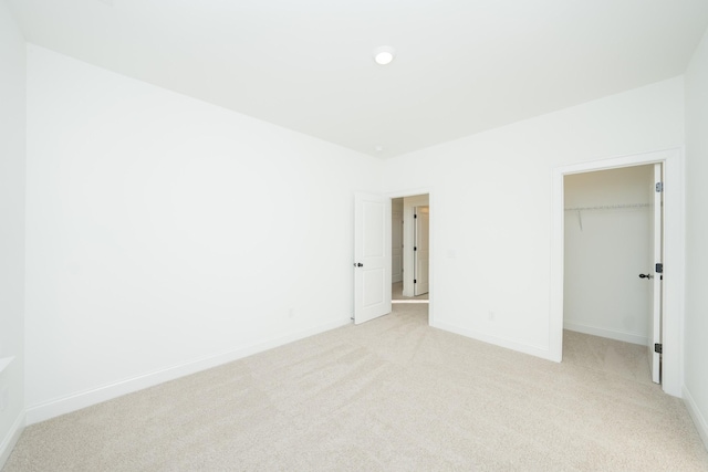 unfurnished bedroom featuring light carpet, a spacious closet, baseboards, and a closet