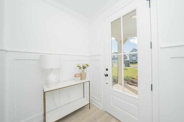 doorway featuring ornamental molding, wainscoting, a decorative wall, and light wood finished floors