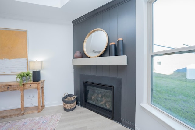 interior details featuring a large fireplace, baseboards, wood finished floors, and crown molding