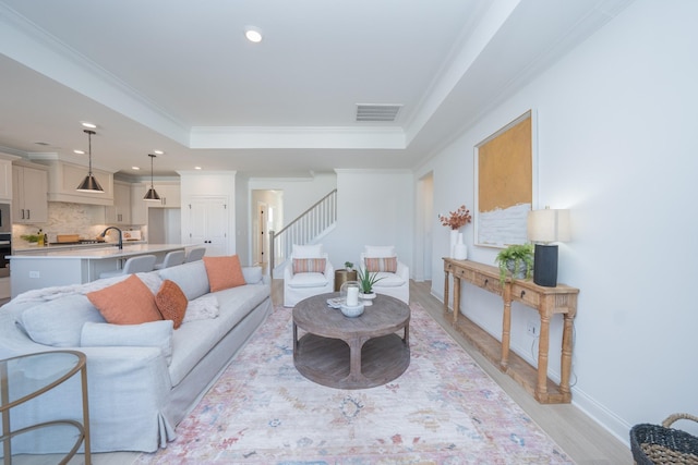 living area featuring ornamental molding, a tray ceiling, visible vents, and stairway