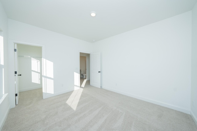 unfurnished bedroom with a walk in closet, light carpet, and baseboards