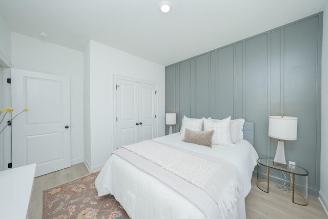 bedroom featuring baseboards, a closet, light wood-type flooring, and a decorative wall