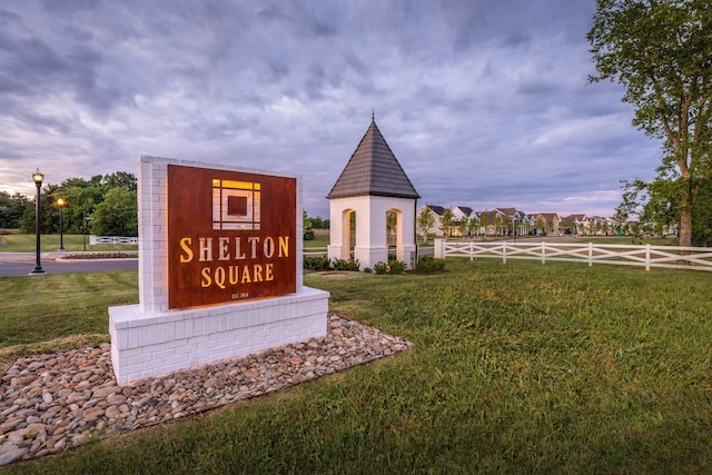 community / neighborhood sign featuring fence and a lawn