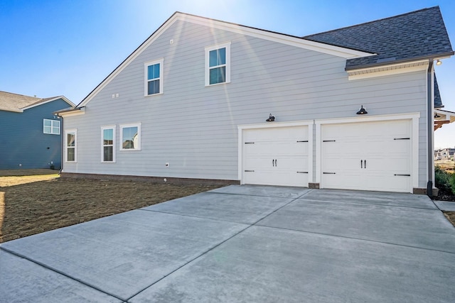 exterior space with concrete driveway and a shingled roof