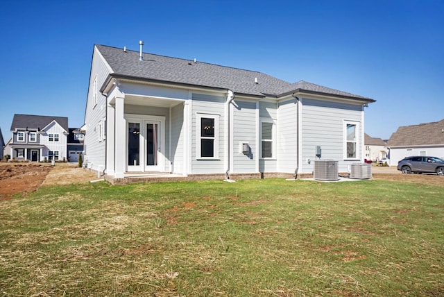 rear view of house featuring a shingled roof, central AC unit, french doors, and a yard