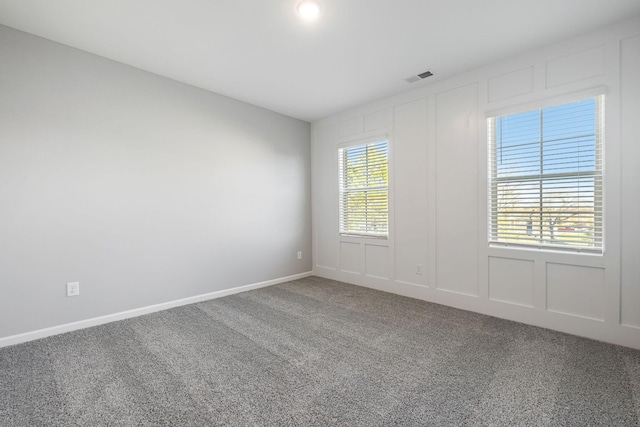 spare room featuring carpet floors, baseboards, visible vents, and a decorative wall