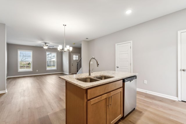 kitchen with light wood finished floors, a sink, an island with sink, light stone countertops, and dishwasher