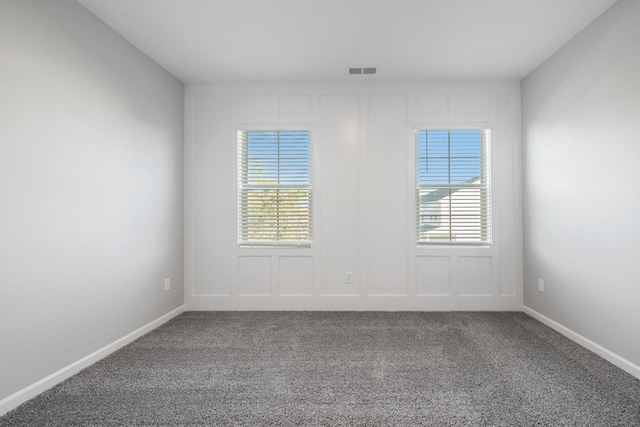 carpeted empty room featuring visible vents, a decorative wall, and baseboards