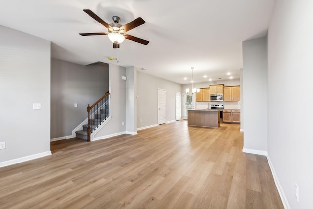 unfurnished living room featuring stairs, ceiling fan with notable chandelier, baseboards, and light wood-style floors