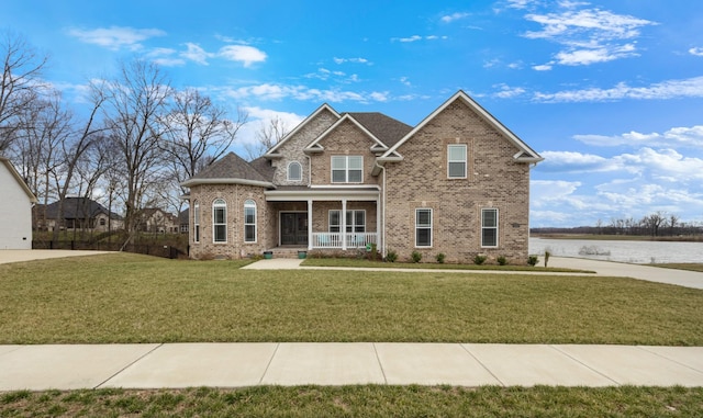 view of front of property featuring a porch, a front yard, brick siding, and a water view