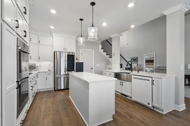 kitchen featuring a center island, dark wood finished floors, decorative columns, appliances with stainless steel finishes, and a sink