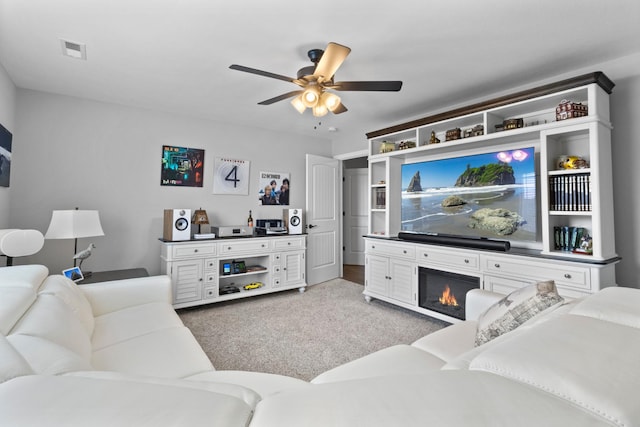 living room featuring light carpet, a glass covered fireplace, visible vents, and a ceiling fan