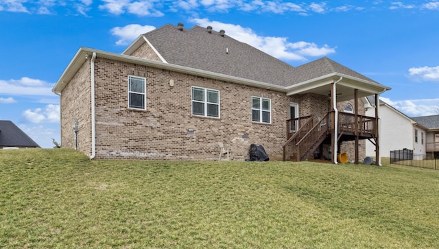 rear view of property featuring brick siding, a shingled roof, fence, stairs, and a lawn