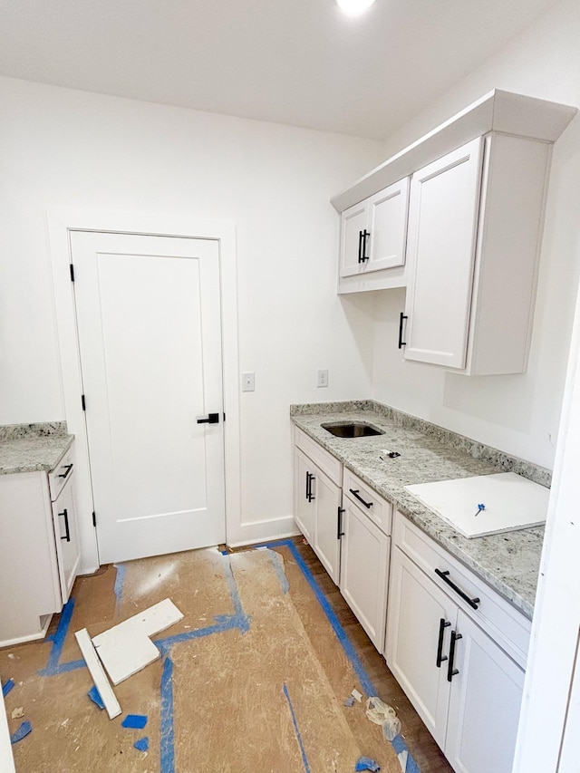 kitchen with light stone countertops, white cabinets, and a sink