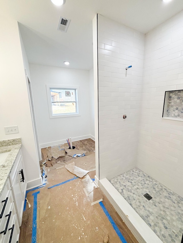 full bath with baseboards, visible vents, a tile shower, and vanity