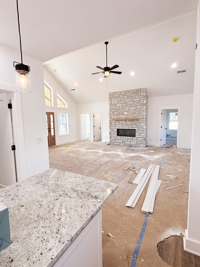 unfurnished living room featuring a wealth of natural light, visible vents, ceiling fan, and a stone fireplace