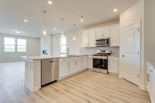 kitchen with visible vents, appliances with stainless steel finishes, a peninsula, light wood-type flooring, and a sink