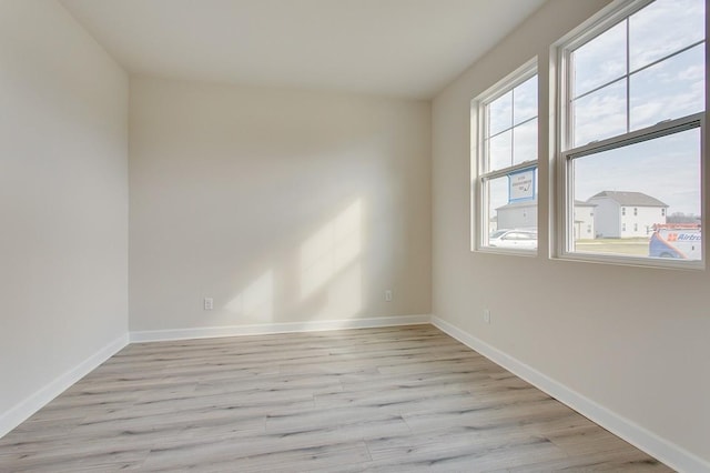 spare room with light wood finished floors, a wealth of natural light, and baseboards