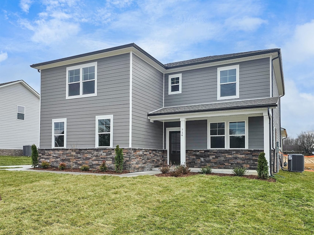 traditional-style house with stone siding, central AC unit, and a front lawn