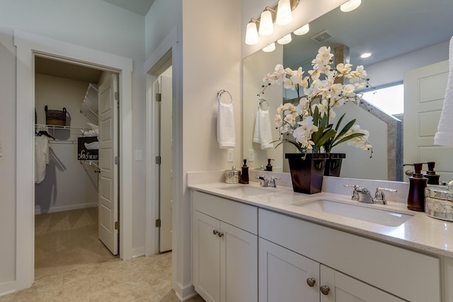 bathroom featuring a walk in closet, visible vents, a sink, and double vanity