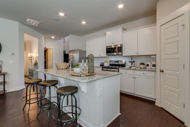 kitchen with dark wood finished floors, stainless steel appliances, recessed lighting, white cabinetry, and an island with sink