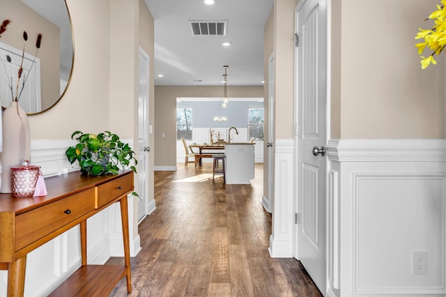 hallway with a decorative wall, a wainscoted wall, recessed lighting, dark wood-style flooring, and visible vents